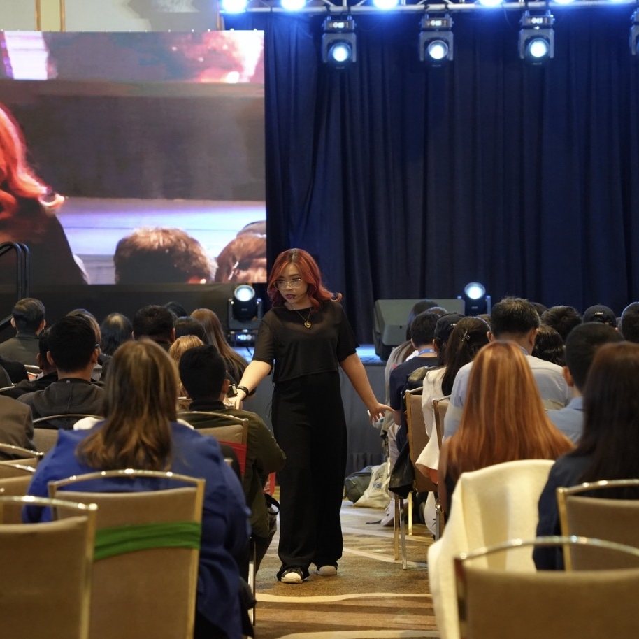 Nikki speaking among the audience, her face on the big screen behind her